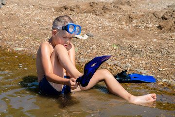 little diver puts on fins while sitting on the shore