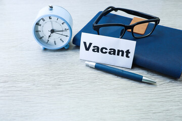 Vacant sign with a pen, eyeglasses on the notebook and alarm clock on wooden table 