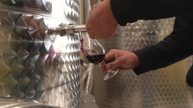 A man pours red wine from the stainless steel vat and spill it everywhere