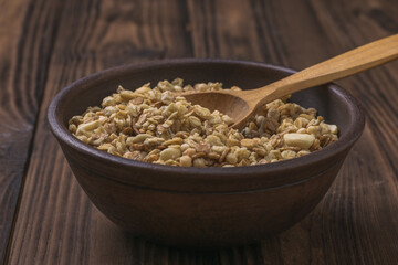 A clay bowl with granola and a wooden spoon on a wooden table.