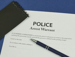 Police Arrest Warrant form with police notebook and pen.