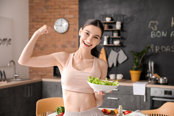 Beautiful young woman eating vegetable salad in kitchen