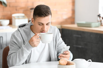 Handsome young man with mobile phone drinking tea at home