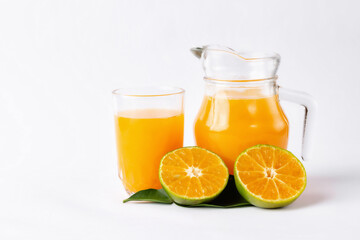 Jug, glass of orange juice and orange fruits with green leaves  on white background