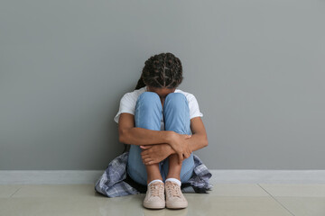 Sad African-American girl sitting near grey wall. Stop racism