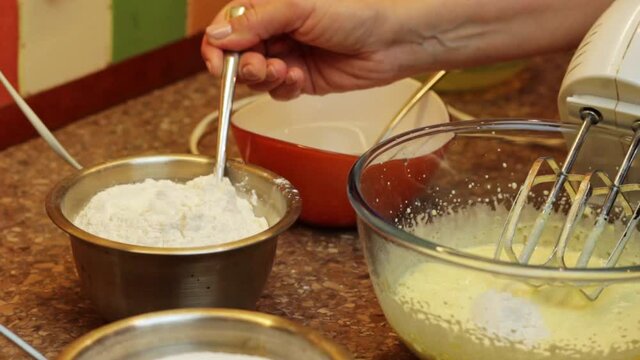 Hand adding flour with spoon to mixed egg yolk, preparation of sponge cake, closeup