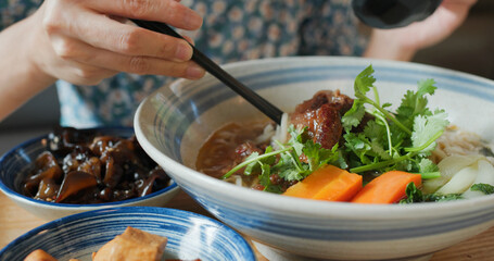 Woman eat taiwanese braised beef noodles bowl in restaurant