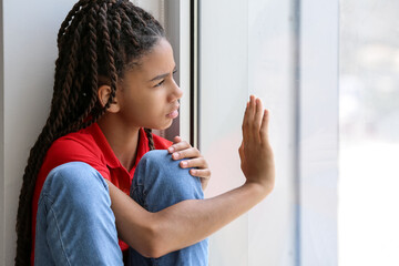 Sad African-American girl sitting on windowsill. Stop racism