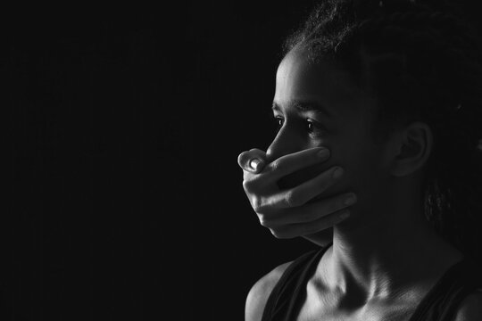 Person covering mouth of sad African-American girl on dark background. Stop racism