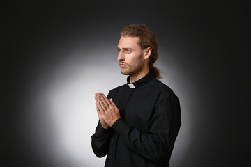 Handsome praying priest on dark background