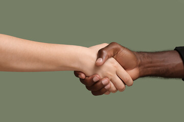 Caucasian woman and African-American man shaking hands on color background. Racism concept