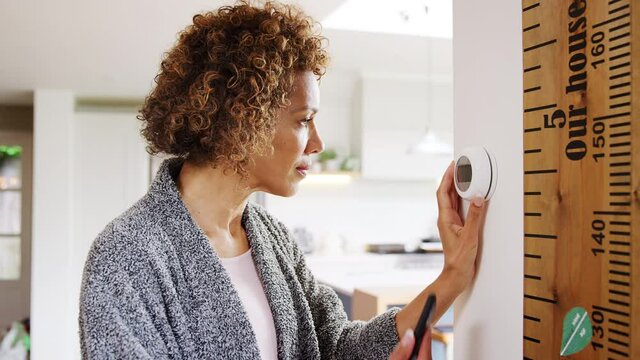 Mature woman using app on phone to control digital central heating thermostat at home with gay partner in background - shot in slow motion