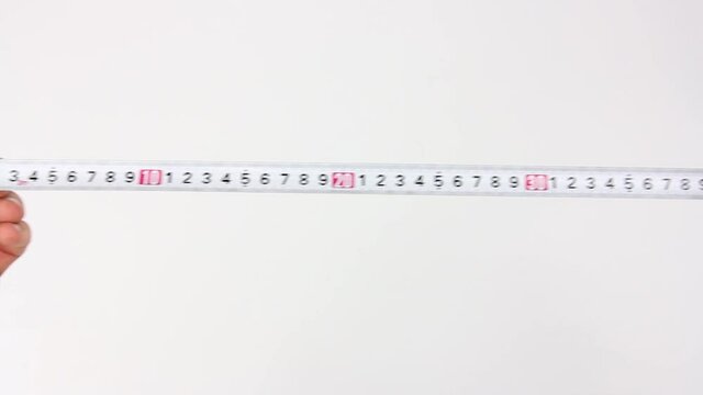 human hands slowly pull the measuring tape out of tape measure and measure the length or width or dimensions, then release the tape and it fast drives back in, close up view on white background
