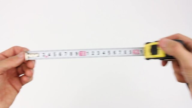 human hands pull the measuring tape out of tape measure and measure the length or width dimensions, then removes from frame, close up view on white background