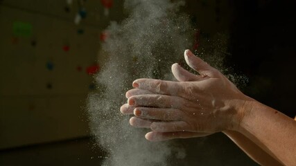 SLOW MOTION, CLOSE UP, DOF: Unrecognizable woman claps her hands after chalking up at climbing gym. Athletic girl indoor climbing slaps her hands together to remove excess magnesium off her fingertips