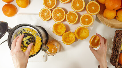Freshly squeezed orange juice. Caucasian woman squeezing oranges using electric juicer. Close up on...