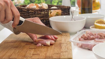 Woman chopping fresh raw chicken meat close up on a wooden cutting board on a kitchen table