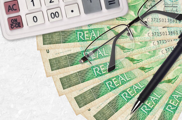 1 Brazilian real bills fan and calculator with glasses and pen. Business loan or tax payment season...