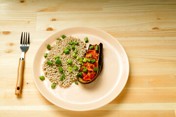 Green buckwheat with baked eggplant with tomato and garlic on a plate with a fork.