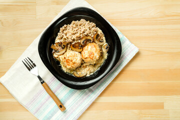 Chicken meatballs with mushrooms in a creamy sauce with green buckwheat in a plate on a linen napkin.