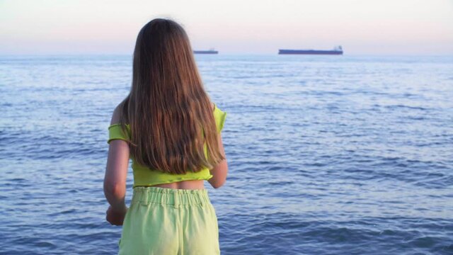 Young girl throwing stones to sea water on cargo ship landscape. Tourist girl throwing rocks to sea water on evening sunset background