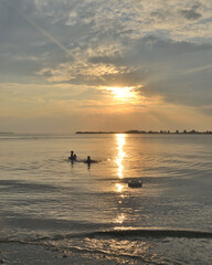 Silhouettes of people in the water against the backdrop of the magnificent sunset sky and the sea.