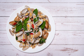 Stir fried Clams with roasted chili paste in white dish on the white wood table.