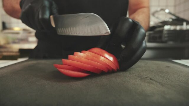Slicing A Juicy Tomato On A Black Cutting Board In A Diner. 
Chef Ably Slices Vegetables.