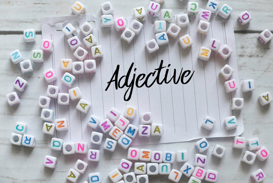 Top view of alphabet beads and paper written with Adjective on white wooden background.