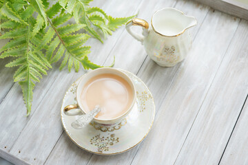 Traditional five o'clock English tea in an elegant china set. Cup of tea with milk and milk jug on a wooden tray. Top view.