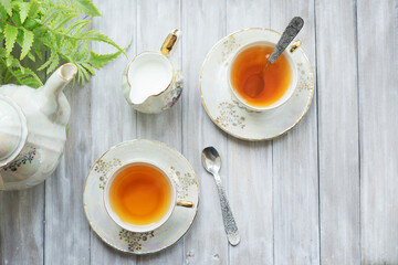 Traditional five o'clock English tea in an elegant china set. Two cups of tea and milk on a wooden vintage tray. Flat lay.