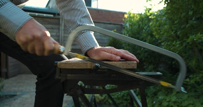 Close Up Of A Man In Striped Shirt Sawing A Metal Rod In Outside Garden At Home