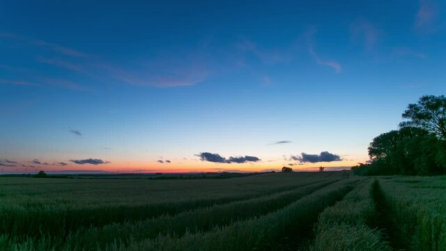 Paths going through green farmlands in Zlotoryja, Poland with the fiery sunset in the background - time lapse