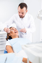 male Dentist is treating patient which is sitting in dental chair in clinic