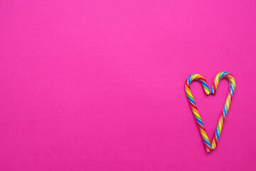 multicolored candy canes in the form of a heart on a pink background, copy space