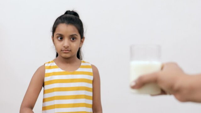 Medium shot of a young Indian kid saying no to the milk given by her mother. A cute little girl sadly waving her hands while looking at a glass of milk  refusing to drink it - lifestyle kids concept 