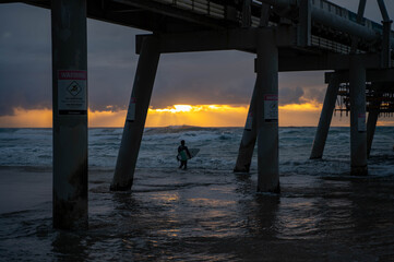Surfer in the ocean at the pier at sunrise