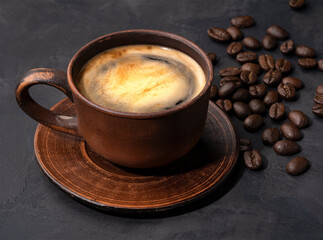 hot coffee with foam in a ceramic cup on a dark background with beans