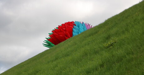 Flagi w kolorze flagi Białorusi ułożone w dekoracyjną dużą kulę na pochyłym stoku porośniętym zieloną trawą, na tle szarego nieba