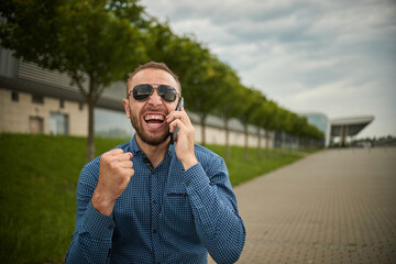 Expanding his empire using technological resources. Man is talking on the phone and smiling at work, happy male speaking mobile telephone in city. Conversation by smartphone outside.