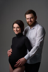 A pregnant woman and her husband are hugging on a gray background. Couple expecting a baby.