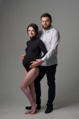 A pregnant woman and her husband are hugging on a gray background. Couple expecting a baby.