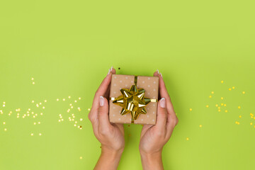 Women hands holding a gift or gift box decorated with confetti on a green table top view. Flat composition for birthday or wedding.