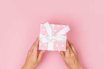 Hands holding craft paper gift box with a gift for Christmas, New Year, Valentine's Day or anniversary on a pink background, top view