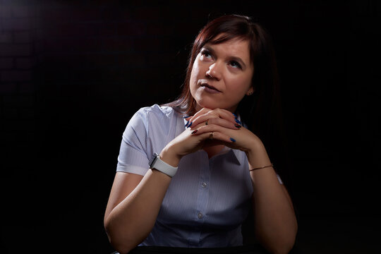 Emotional portrait of caucasian brunette girl or middle aged woman with long dark hair in blue shirt on black background and interesting light from flash in studio.