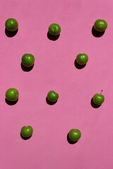 Green plum isolated on pink background. Still life photography.	