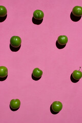 Green plum isolated on pink background. Still life photography.	