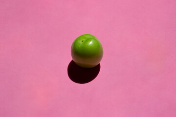 Green plum isolated on pink background. Still life photography.	