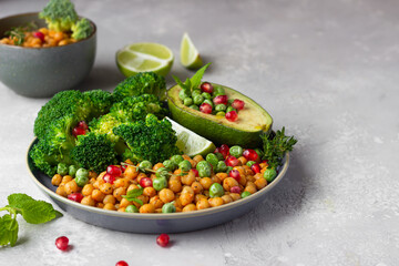 Healthy vegetable lunch of broccoli, roasted chickpeas, avocado, green peas, pomegranate seeds, lime and mint on a ceramic plate. Vegan food, clean eating or dieting concept.