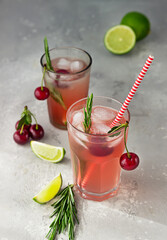 Cocktail or lemonade with cherries, lime and rosemary on a grey concrete table. Summer refreshment drink.